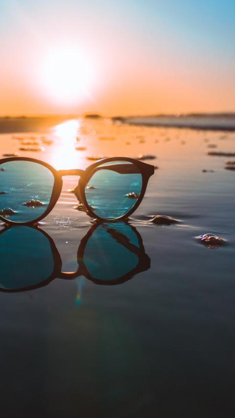 Stylish sunglasses on beach reflecting sunset – fashion eyewear for summer vacations